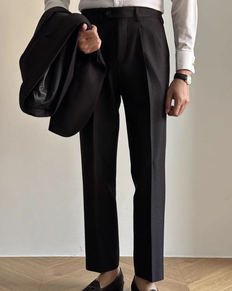 A person indoors models CjDropshipping’s Orta Tailored Trousers – Four Seasons Elegance with a white long-sleeve shirt, holding a black jacket. Black loafers and a watch complete the look; their face remains unseen.